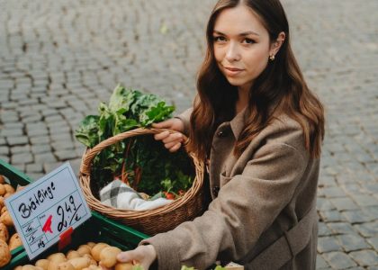Young woman shopping at Erfurt farmers market, holding basket with fresh vegetables. Capturing local shopping culture.
