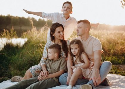 A family of five enjoying a serene picnic in a sunlit meadow during sunset.