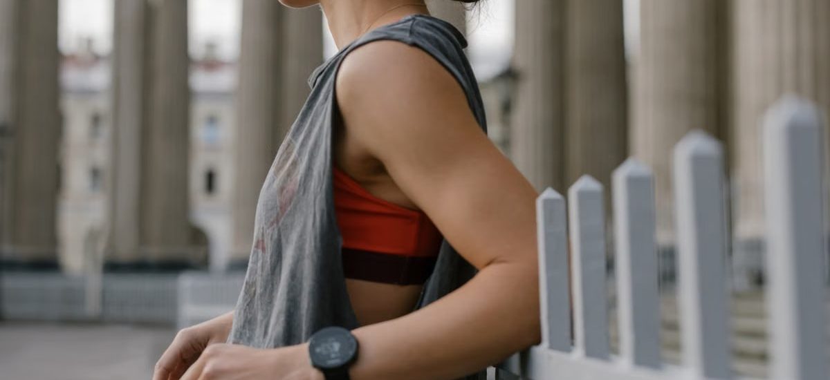 A woman in a tank top leans against a railing in an urban setting, wearing a wristwatch.