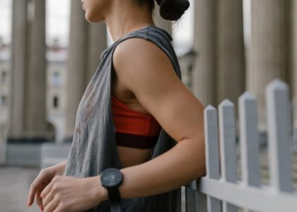 A woman in a tank top leans against a railing in an urban setting, wearing a wristwatch.